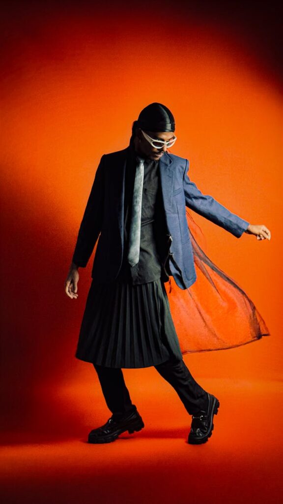 Stylish man in modern attire with an orange background, showcasing unique fashion sense.